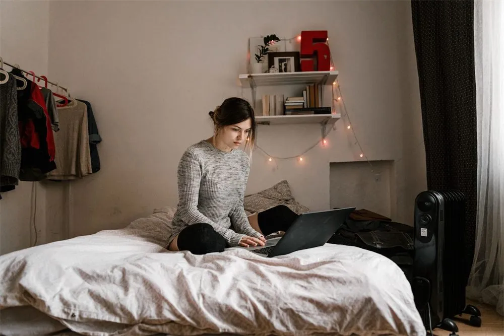 Woman in a thick sweater working on a laptop in a cold bedroom next to a radiator