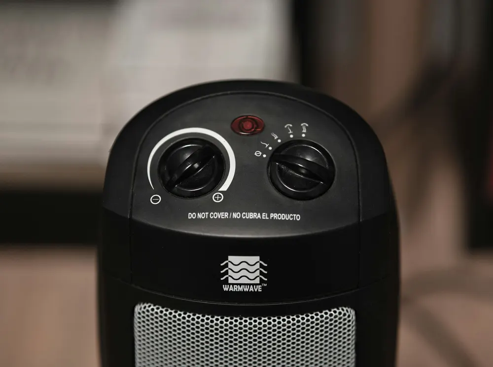 The top of a black ceramic tower heater showing a thermostat dial, a heat setting dial and a power light