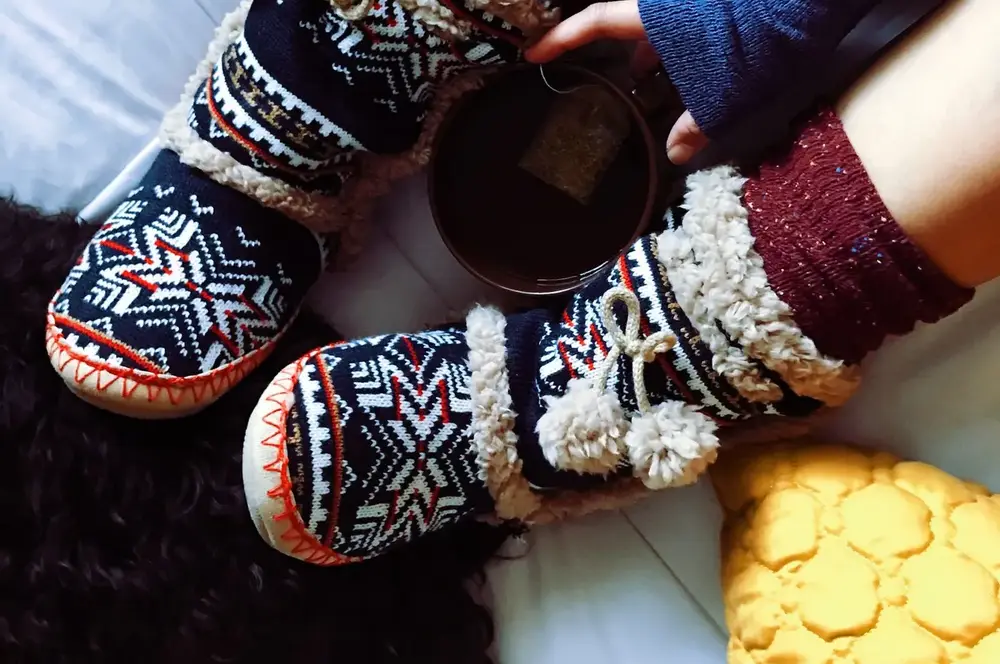 Warm slippers and a cup of tea on a bed in a small, heated bedroom