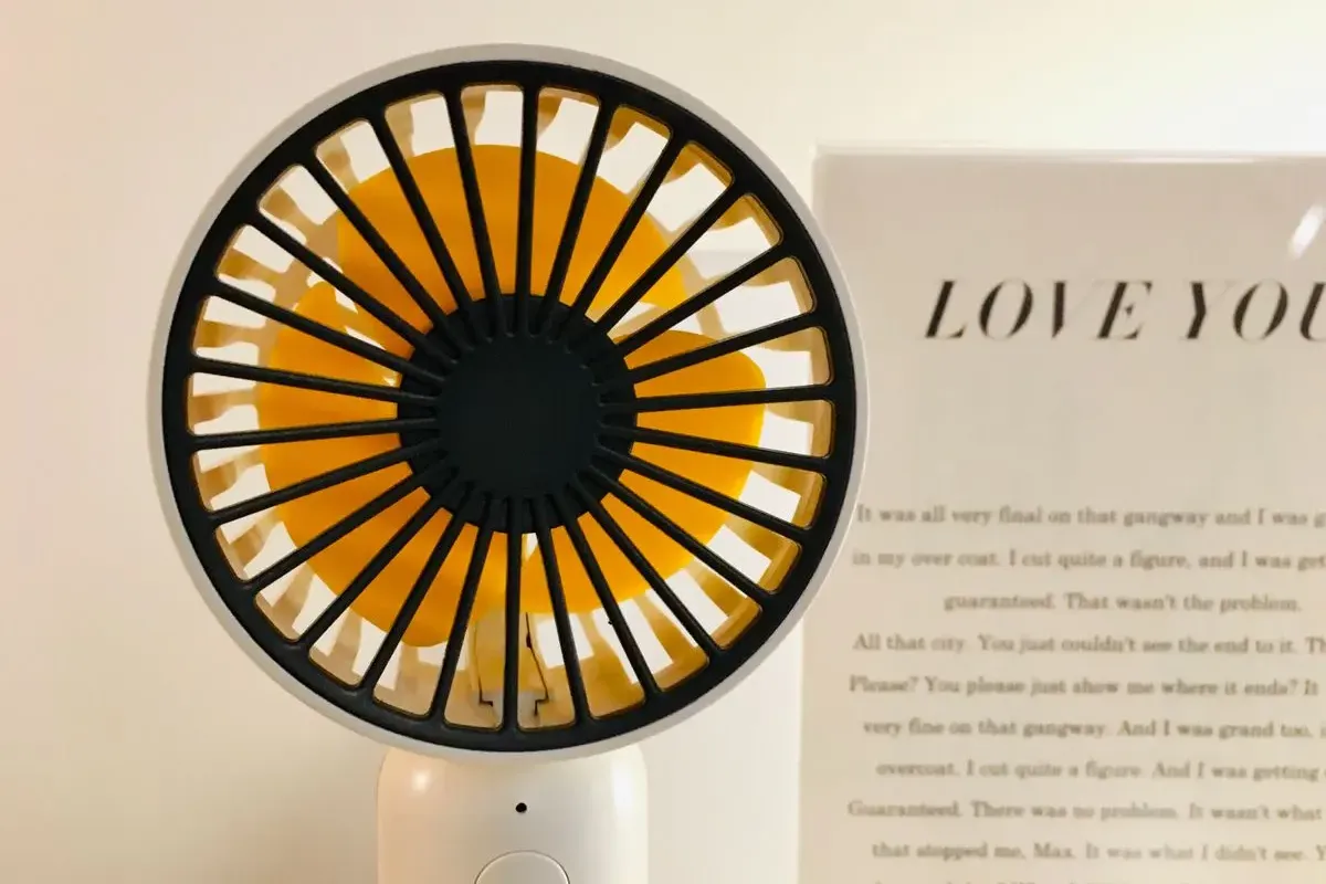 A small white handheld fan standing on a desk, the simplest kind of personal cooling