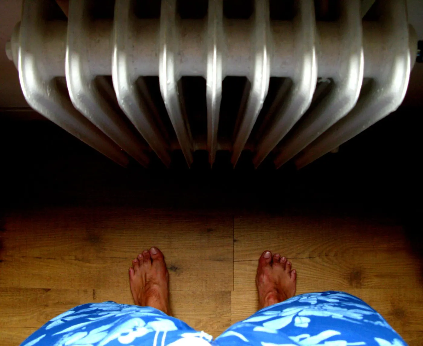 Bare feet on a hard wooden floor in front of a radiator, showing the clear floor space to leave around a heater