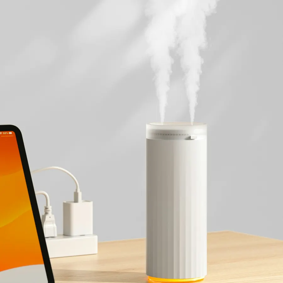 A white cylindrical humidifier releasing two columns of mist on a wooden desk next to a tablet and a phone charger