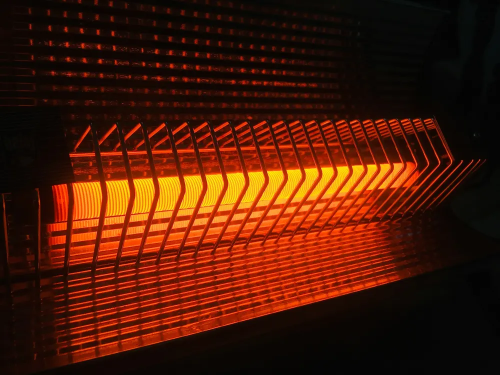 The glowing orange heating element of a radiant electric heater seen in a dark room