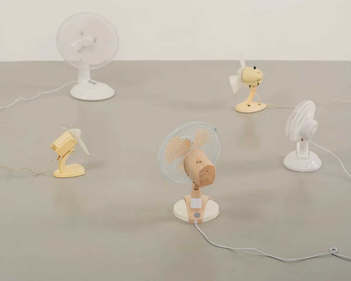 Five small desk fans in different colors standing on a plain floor, showing the personal scale of small cooling devices
