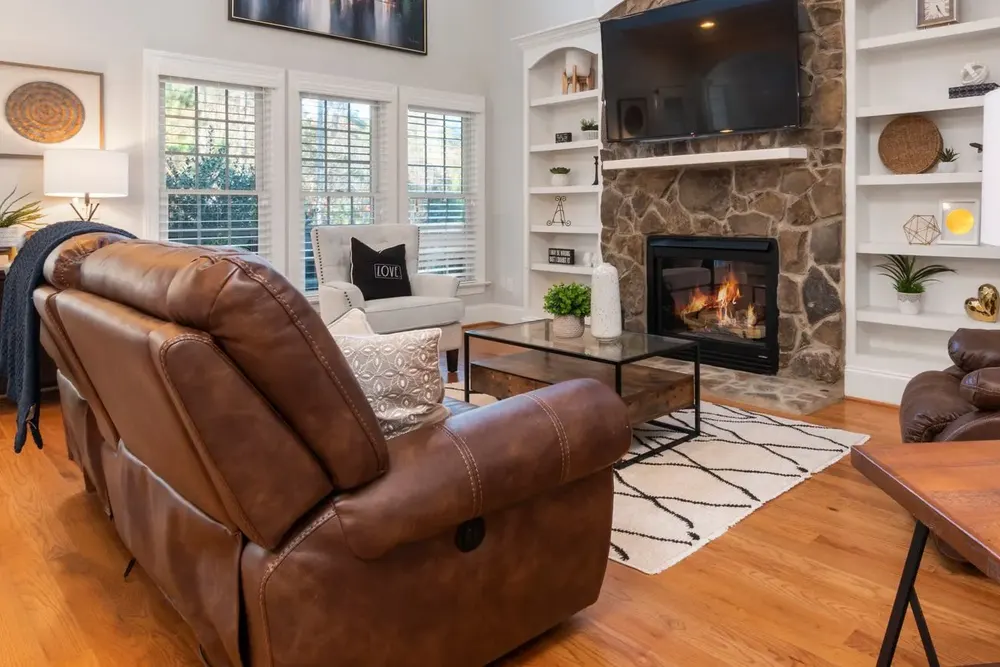 A living room with a leather recliner, a coffee table and a rug arranged around a stone fireplace