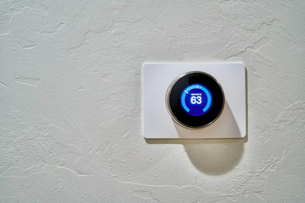 A round digital wall thermostat on a white textured wall, set to 63 degrees