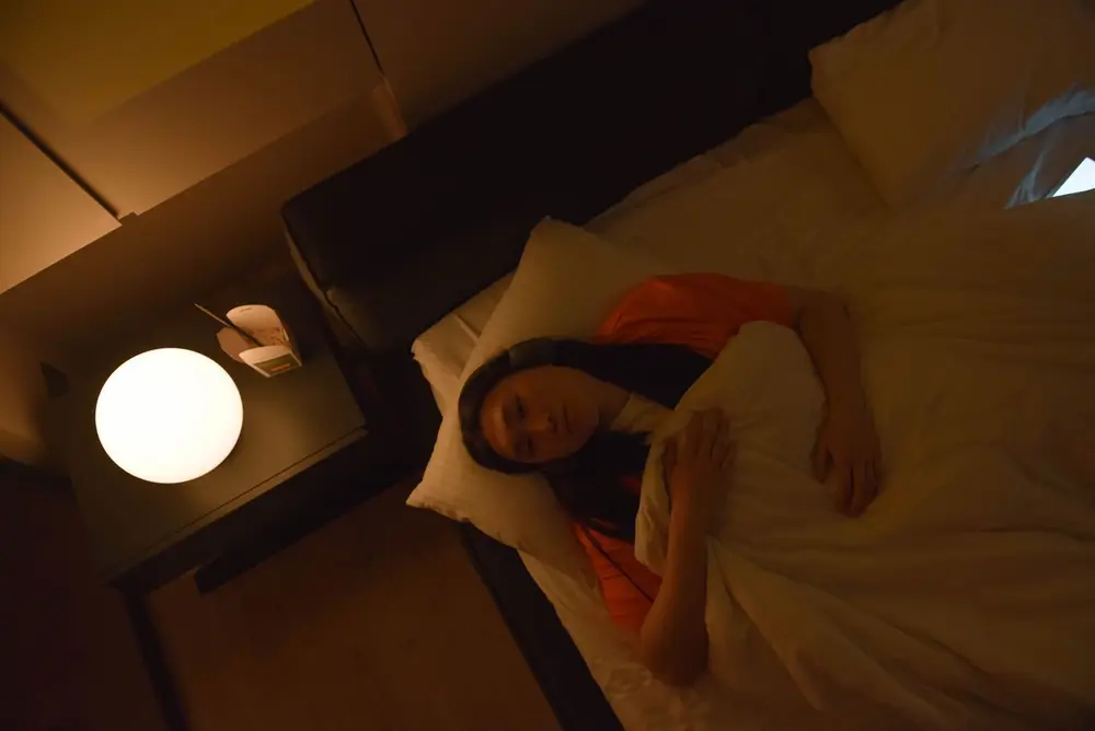 Woman lying awake in bed at night under a warm bedside lamp